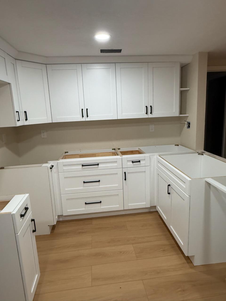 White kitchen cabinets with black handles during installation, before countertops are fitted